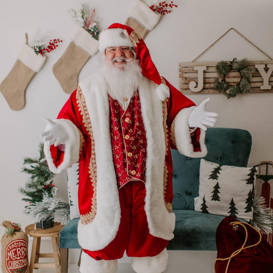 Santa standing in room with greeting arms